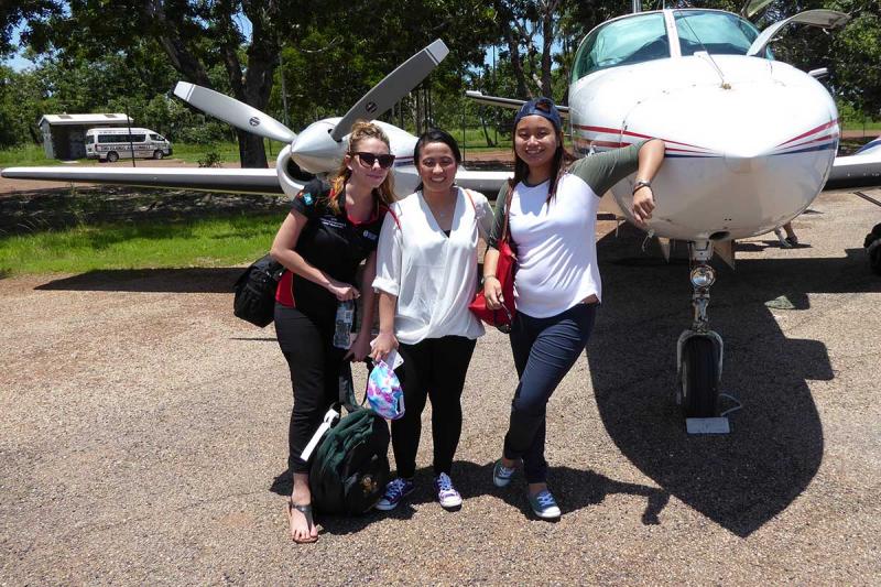 Three young women standing beside a small plane